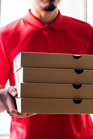A delivery person in a red polo shirt holding a stack of four pizza boxes