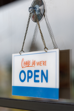 Open sign hanging by a chain from a suction cup on a glass storefront door or window.